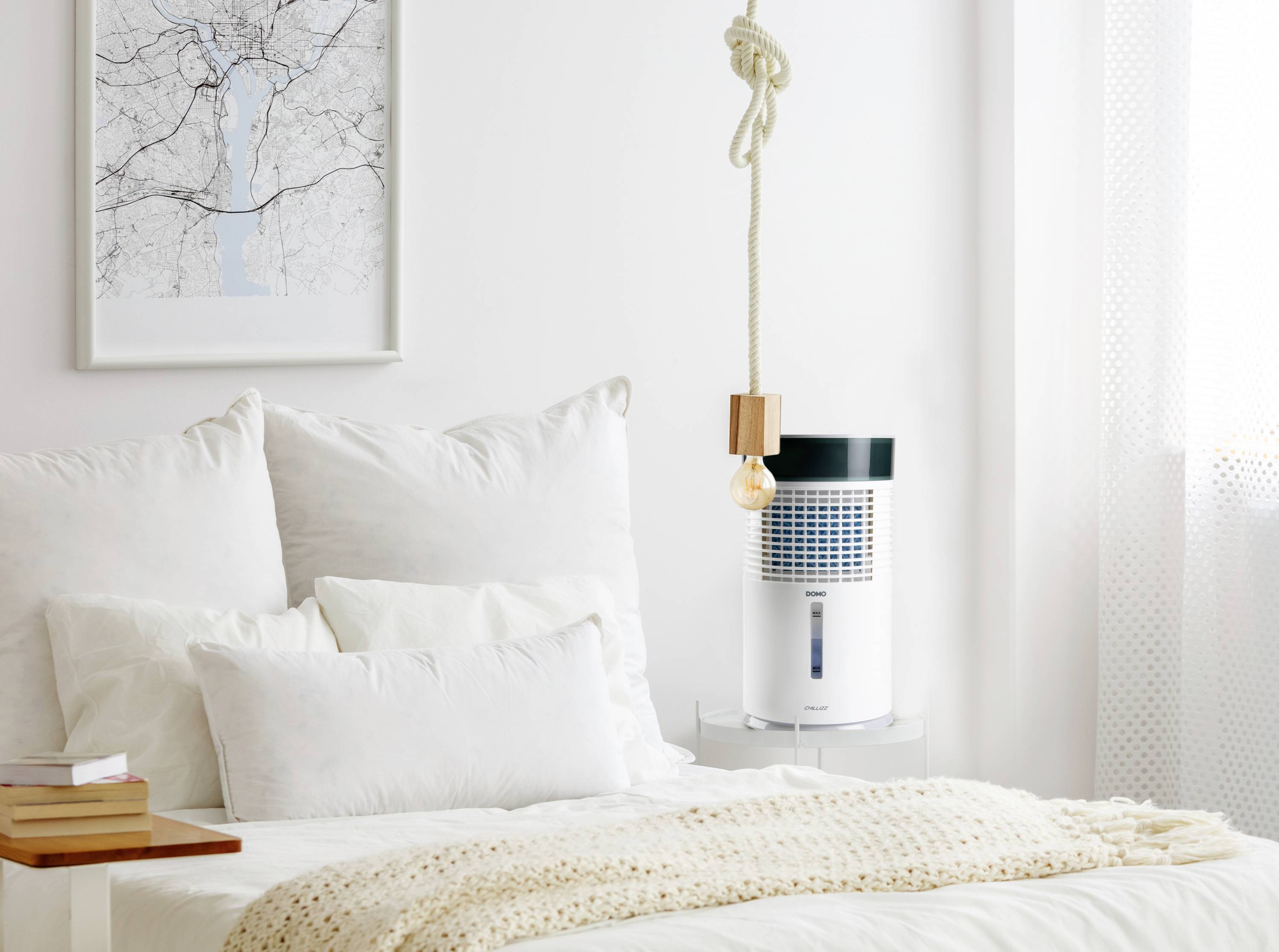 Bright bedroom with a white bed and pillows, an air purifier on a table and a pendant light hanging from a cord. Wall art depicts a tree.