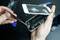 A person is holding a smartphone with a cracked screen, opening it with tools to reveal the internal components. Repair scene.