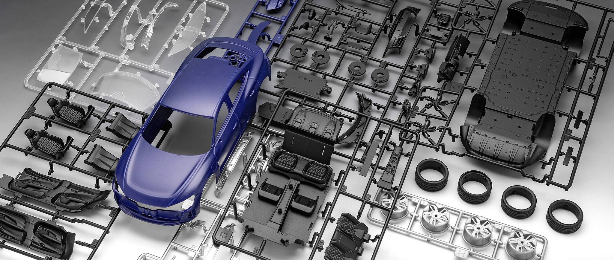 A model kit of a car shows individual components such as bodywork, seats and tyres, arranged on a sprue, ready for assembly.