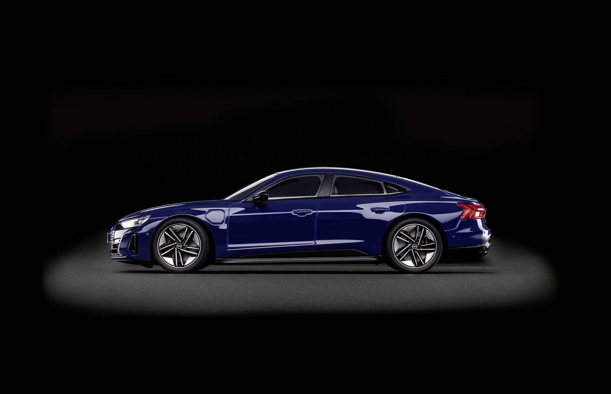 Dark blue electric car stands sideways on a black background. Elegant design with distinctive alloy wheels and aerodynamic lines.