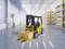 A yellow forklift truck is transporting a crate marked 'Fragile' in a bright, modern warehouse with shelves stacked full of cardboard boxes.