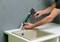 A person is using a cartridge gun to apply sealant around a sink. Hands are holding the gun over the edge of the basin.