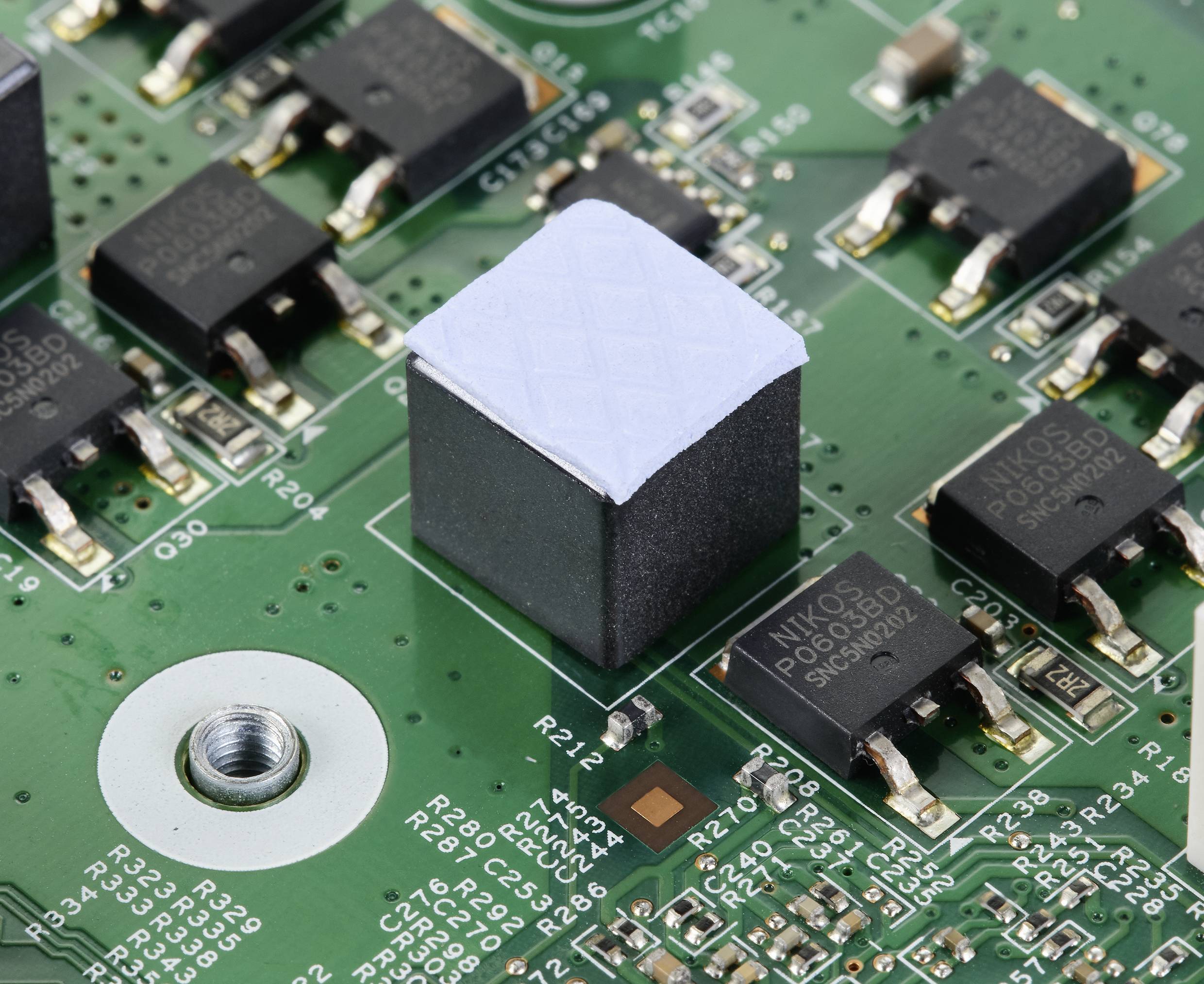 Close-up of a green printed circuit board with several black electronic components and a central, larger square component.