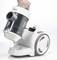 A hand is holding a white vacuum cleaner with a transparent dust container. The vacuum cleaner has large wheels and a modern design.