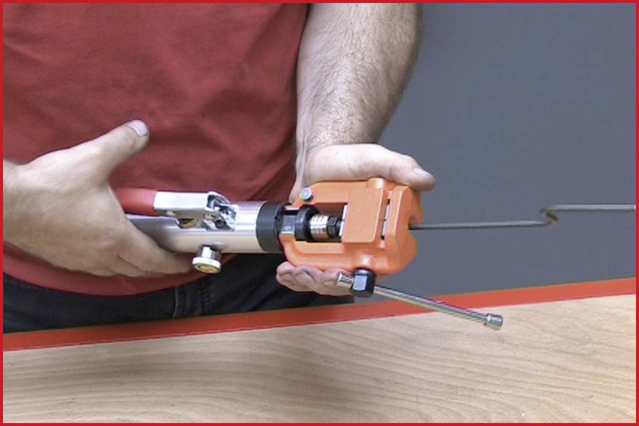 'A person is holding a red handheld device with a long metal attachment, apparently for repair or assembly over a wooden table.'