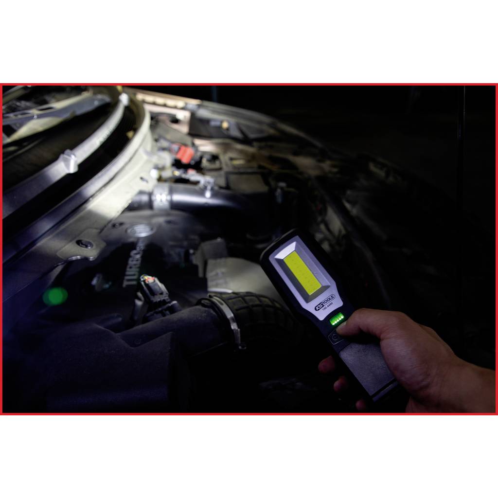 A person is inspecting the engine compartment of a car in the dark with a torch. The torch provides bright light on the engine area.