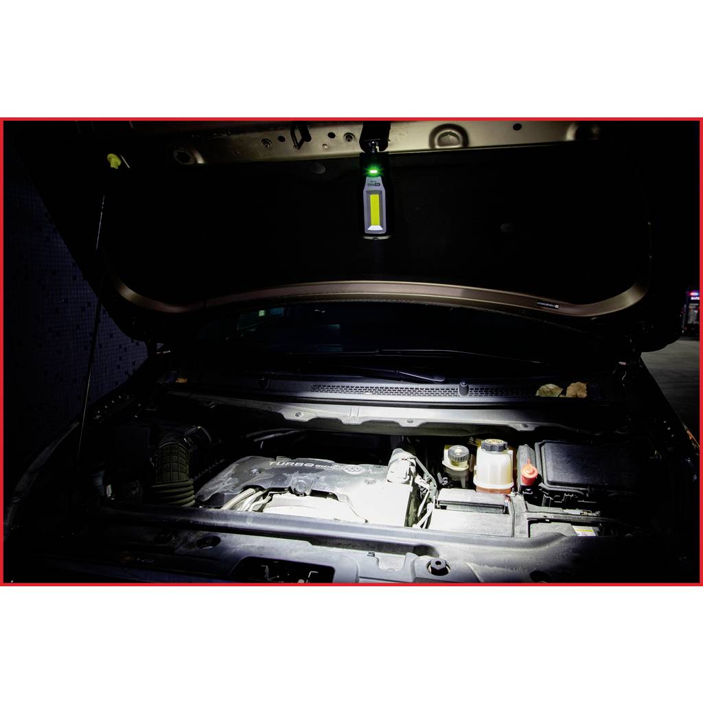 A car with its bonnet raised in a garage. A lamp is shining into the interior, with details of the engine visible.