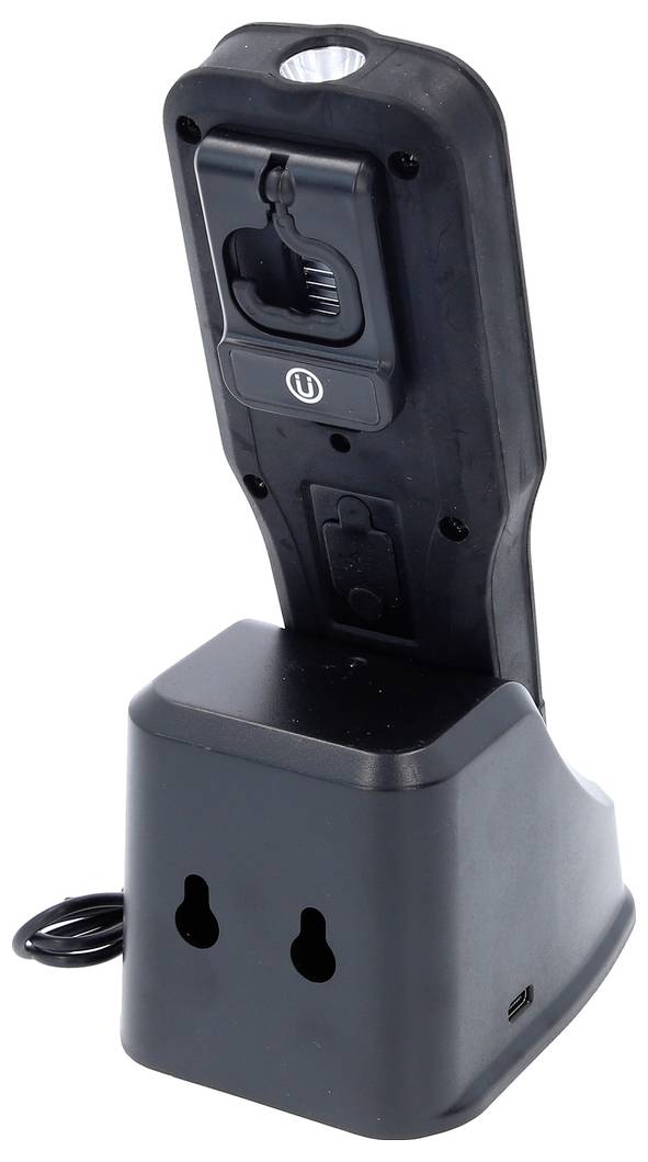 A black electronic device sits in a charging station that resembles two power sockets. A small lamp is visible in the upper area of the device.