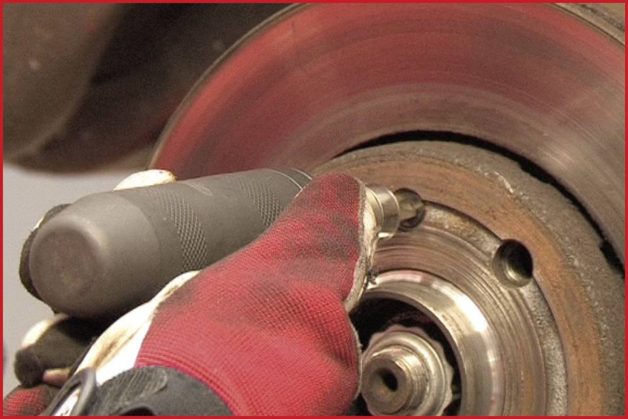 A person is cleaning a brake disc with a tool. The brake disc is rusty and rotating while the person works.