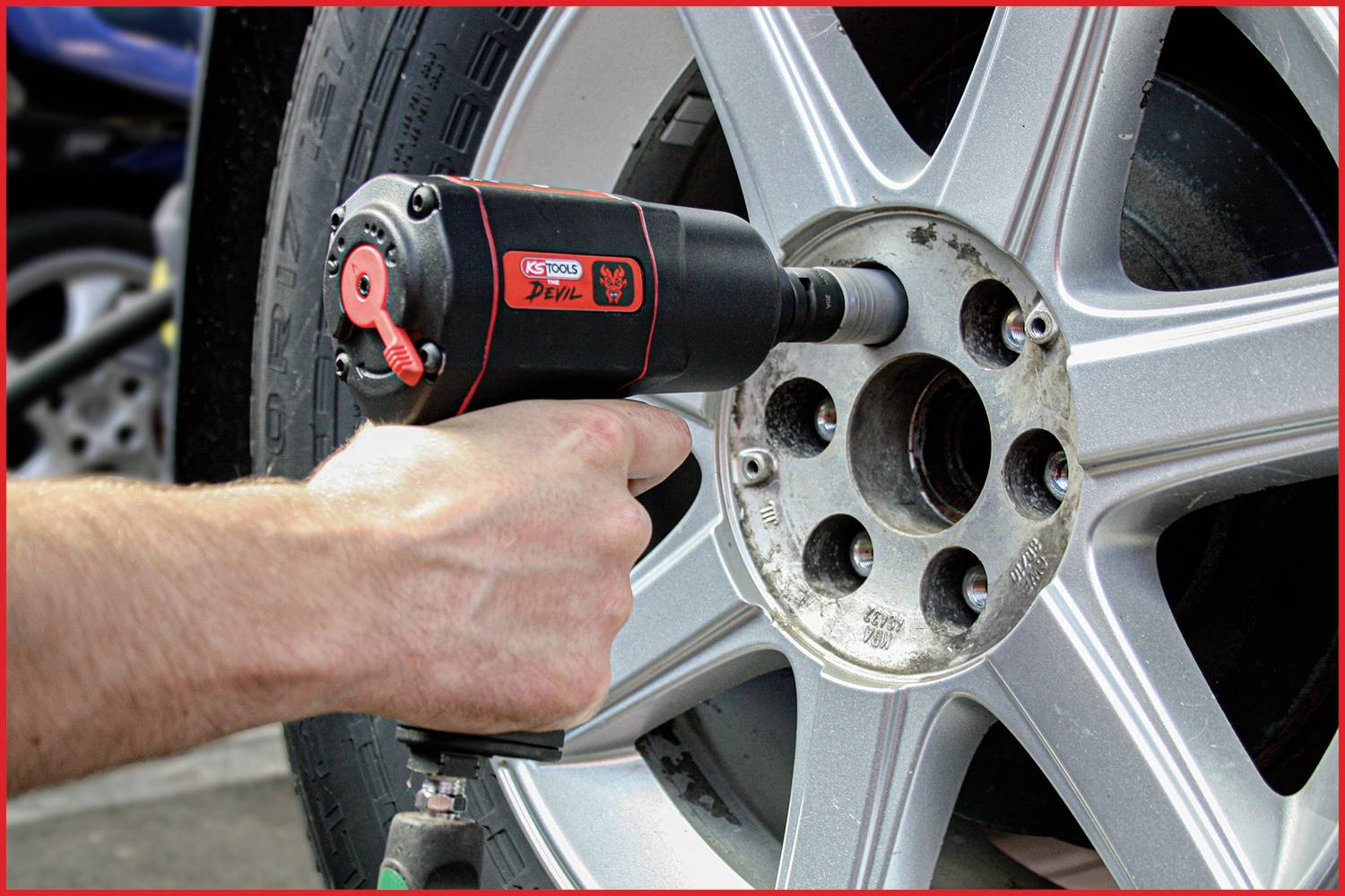 Someone is changing the wheel nuts on a car using an electric impact wrench. The wheel is silver.