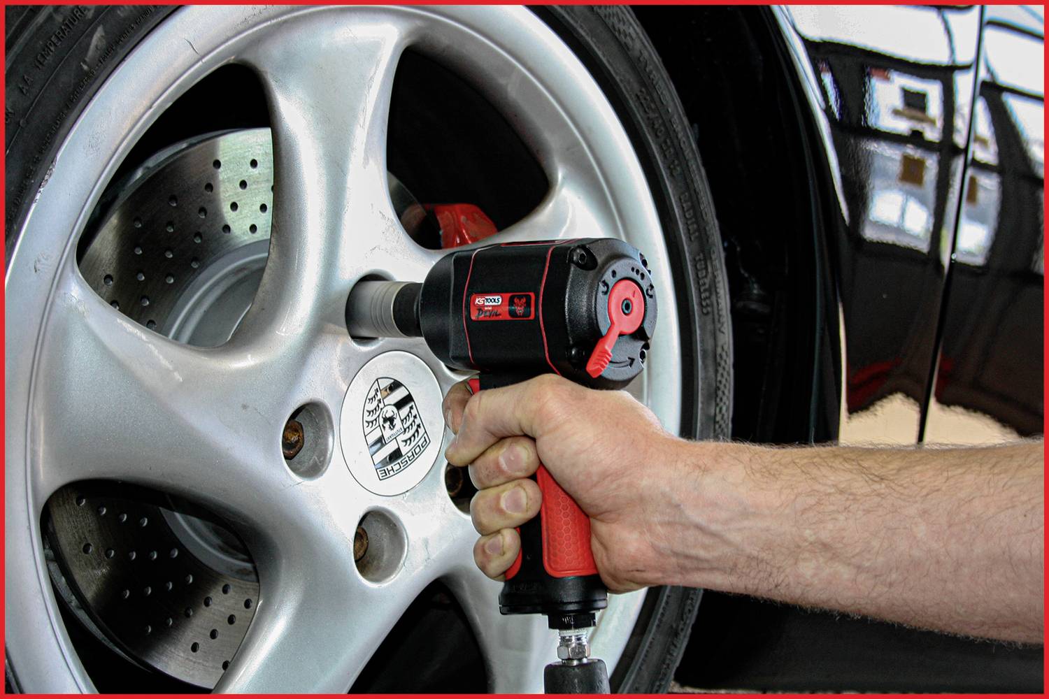 A person is tightening the wheel nuts of a car with an electric impact wrench. The image shows a close-up of the tool in use.