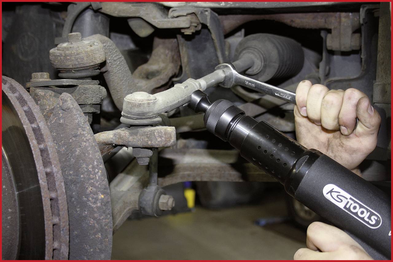 A person is using professional tools to secure an automotive connection. Visible parts of the car suspension are shown in the image.