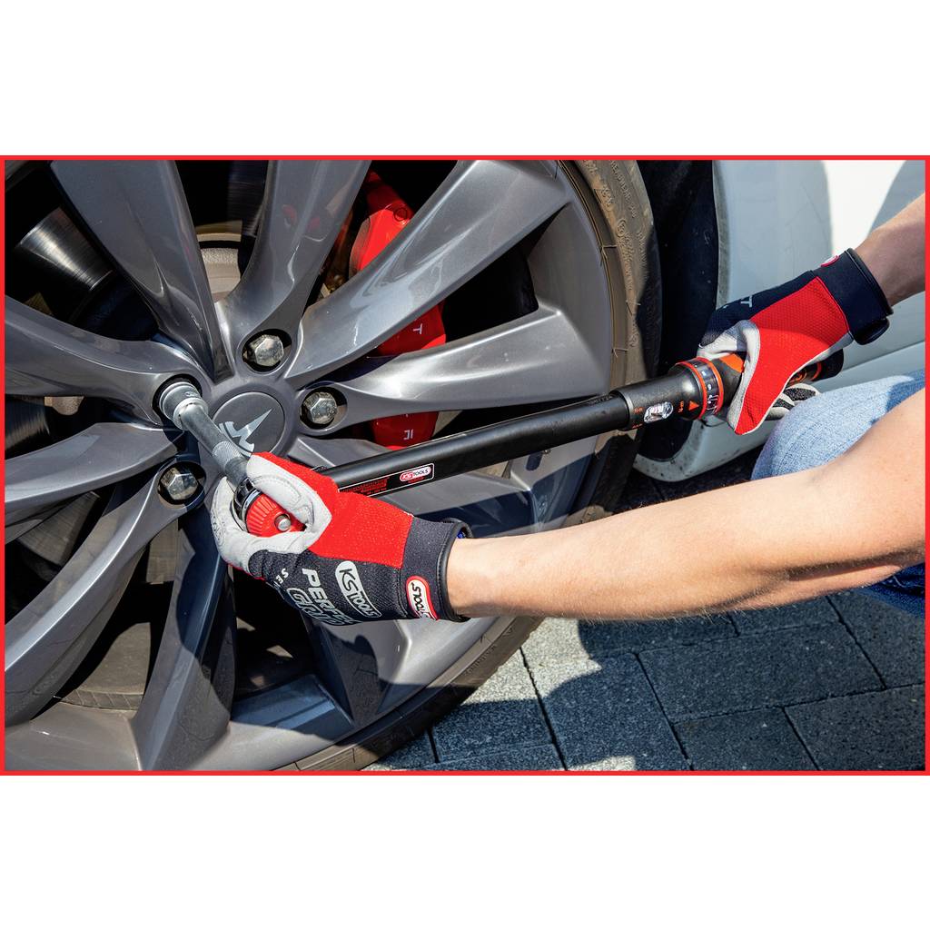 A person is tightening the wheel nuts of a car tyre using a torque wrench. The person is wearing red gloves.