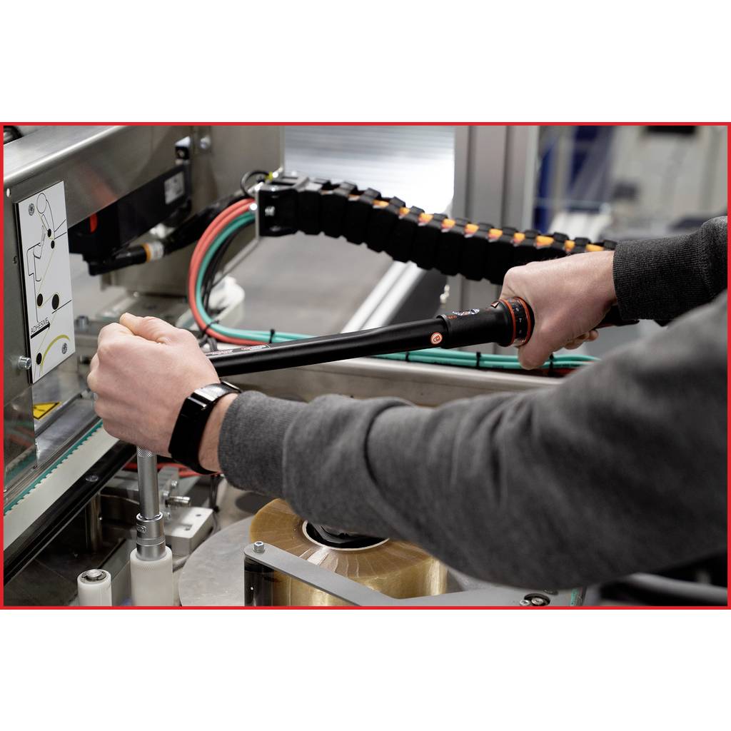 Two hands are operating a device on a machine with wiring. One person is wearing a dark top and a black wristwatch.