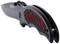 A black folding knife with a red handle pattern and a partially exposed blade lies slightly open.