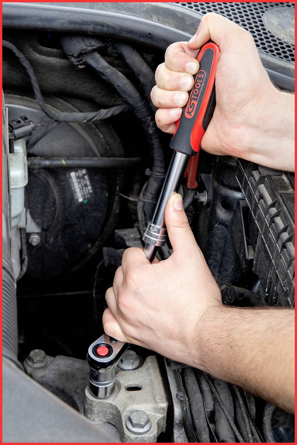 A person is using two hands to tighten a ratchet in an engine compartment. They are holding the tool with a firm grip.
