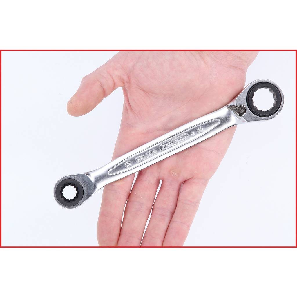 A hand is holding a silver ring key with two sizes. The background is white, and the ring key is reflecting light.