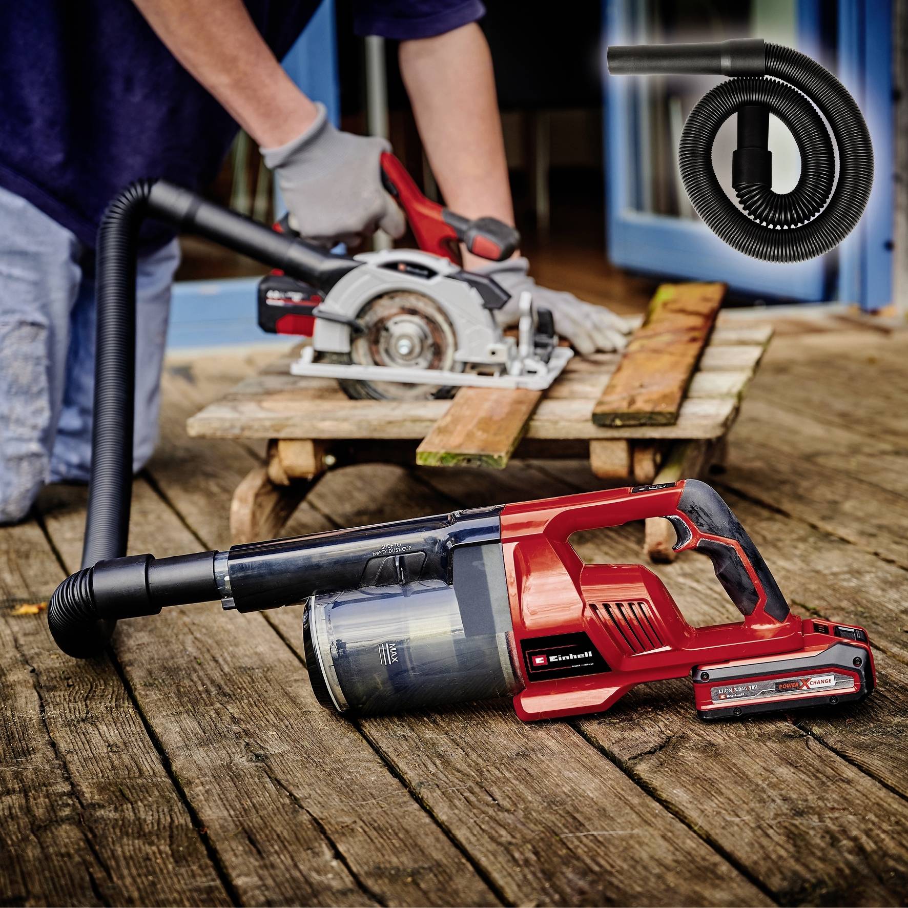 A person is sawing a wooden board with an electric circular saw, while a vacuum cleaner is collecting the sawdust.