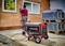 A portable generator stands in the foreground of a construction site. In the background, a person is working on an unplastered house wall.