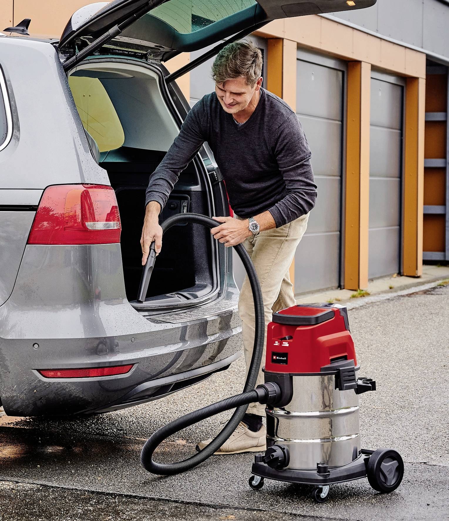 A man is vacuuming the boot of a car with a wet and dry vacuum cleaner in a car park.