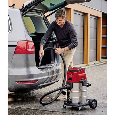 A man is vacuuming the boot of a car with a wet and dry vacuum cleaner in a car park.
