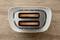 A two-slice toaster, photographed from above, with brown toast slices in the slots. The background is a wooden surface.