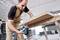 A man is using an electric jigsaw to cut a wooden board in a workshop area. Additional tools are visible in the background.