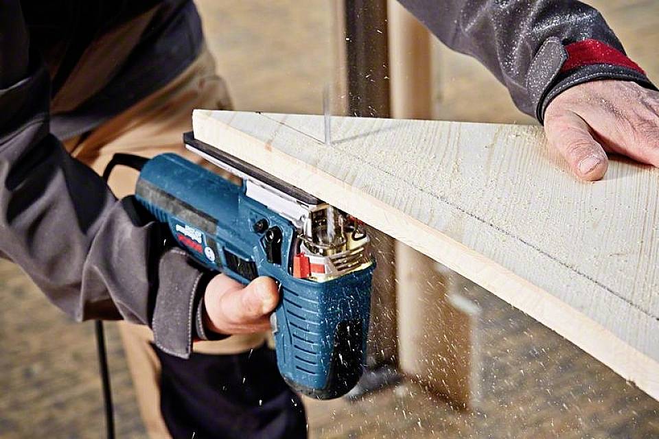 A person is sawing a piece of wood with an electric jigsaw. Wood chippings are flying around.