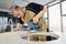 A craftsman is cutting a circular hole in a worktop using a jigsaw in a workshop setting during daylight.