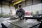 A person is grinding a large metal plate in a factory hall. They are wearing protective clothing and working intently at a workbench.