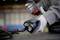 A person wearing grey gloves is holding an electrical tool, ready to work. Background blurred.