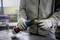 A person wearing work attire and gloves is holding and operating an electric tool for metalworking in a workshop environment.