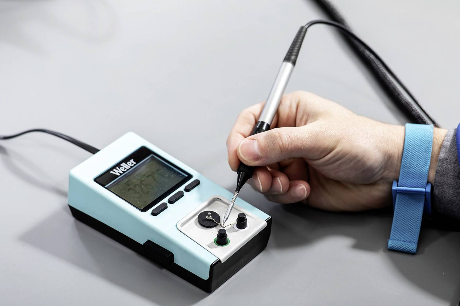 'Hand holding a soldering iron at a soldering station with a digital display and control buttons.'