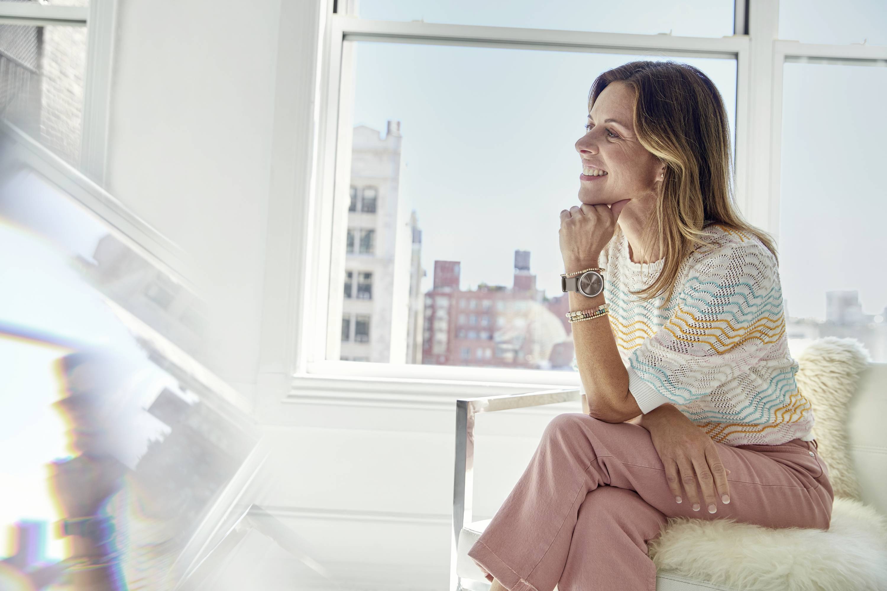 A smiling person sits on a chair in a bright room, gazing out of the window and enjoying the sunbeam on their face.
