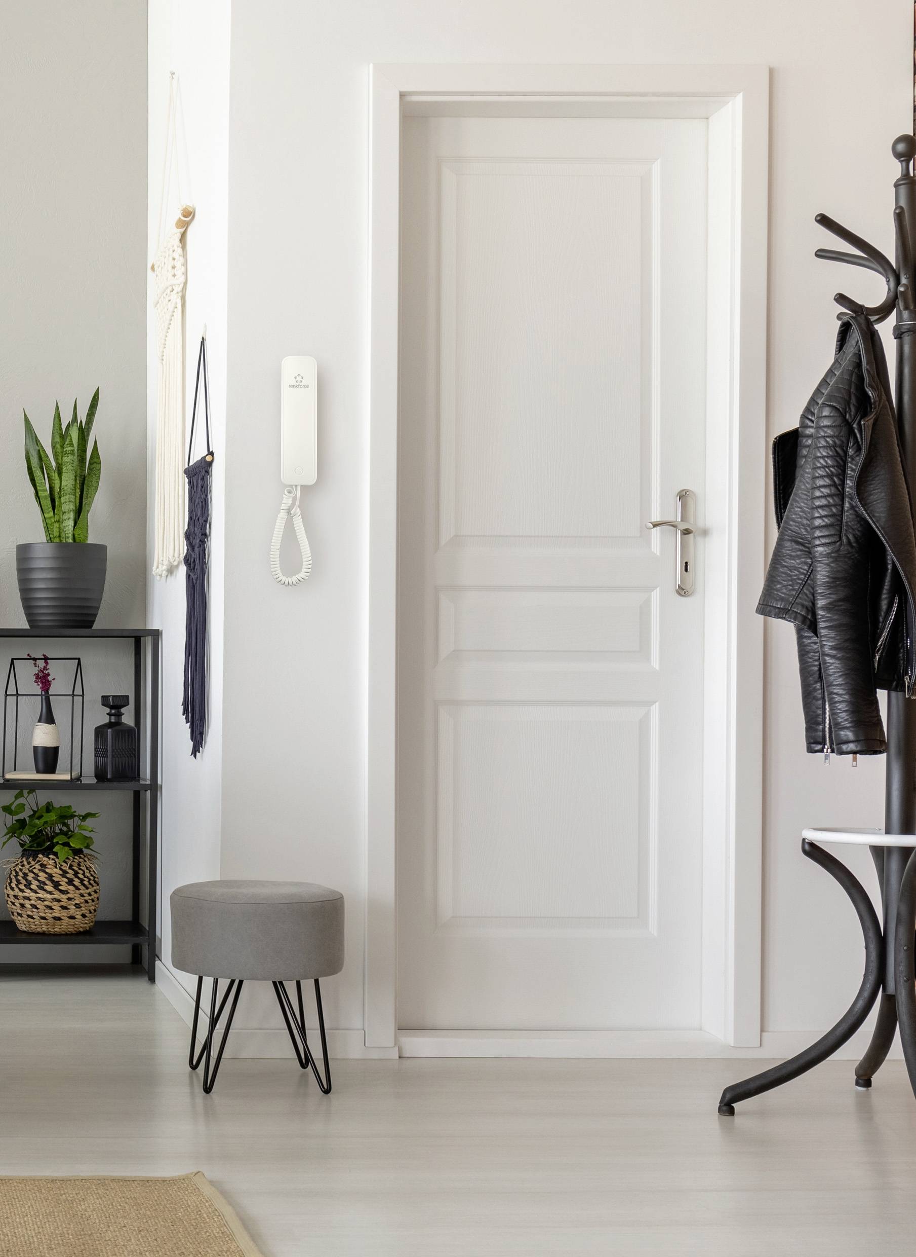 White interior door in a hallway, surrounded by plants, a small stool and a dark brown coat rack with a leather jacket.