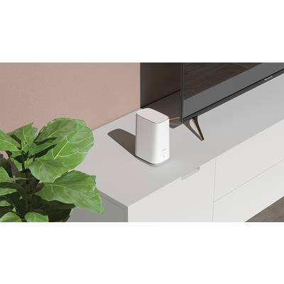 A white router sits on a modern, light grey cabinet, next to a green plant and a television.