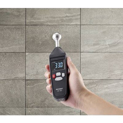 A hand holds a digital measuring device in front of a wall with beige tiles. The display shows '3.30'.