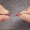 Two hands are holding a violet-sheathed cable with a stripped end and a red crimping connector against a grey background.