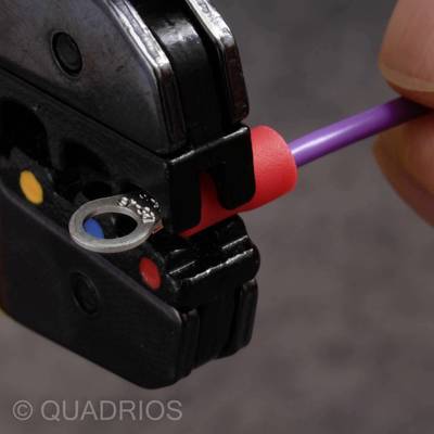 Close-up of a crimping tool securing a red cable lug to a purple wire. A hand is holding the wire.
