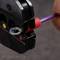 A hand is holding a purple wire, which is being processed with a crimping tool. The tool has coloured markings.