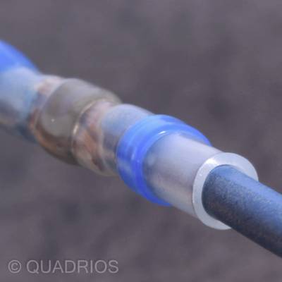 A blue cable is connected with heat-shrink tubing. The background is out of focus. The aim is electrical insulation and connection.