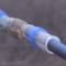 A blue pipe section connected by a transparent flexible coupling, against a blurred grey background, demonstrates a connection technology.