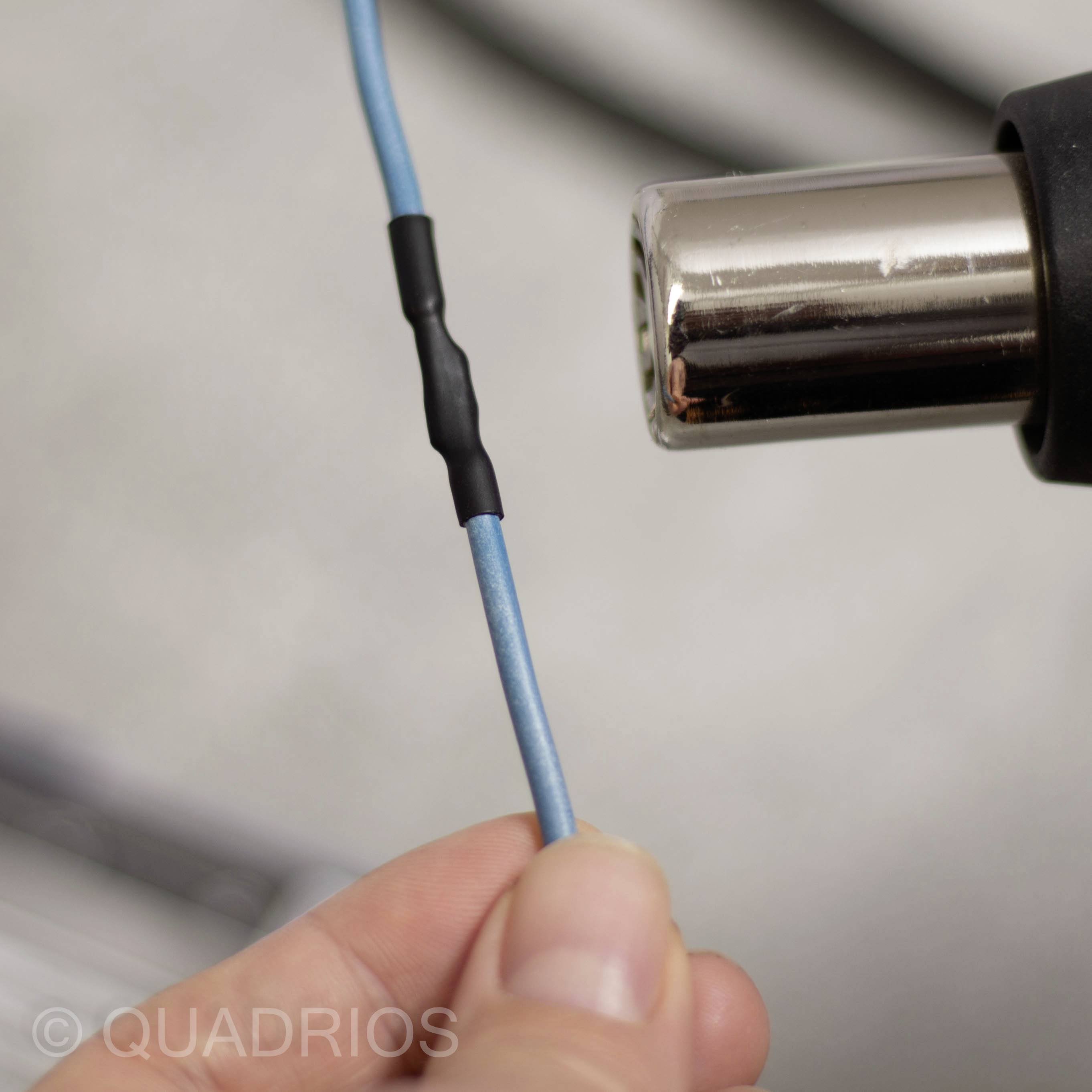 A hand holds a blue cable with a black sheath, which is being plugged into a shiny metal connector.