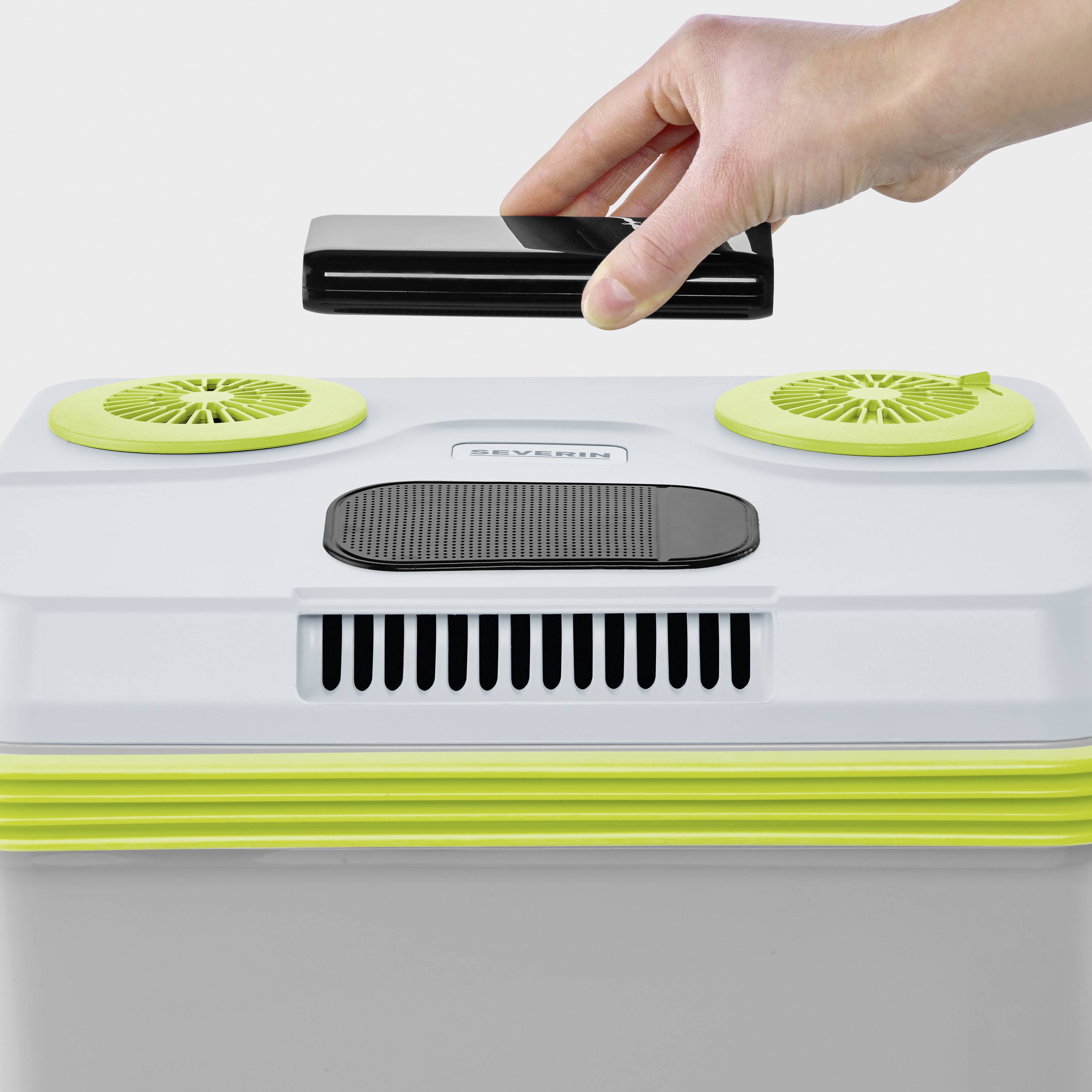 A hand is holding a smartphone over an air purifier with green fan covers, which is standing on a white background.