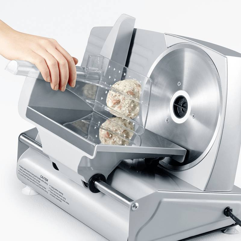 'A person is slicing dough with an electric bread slicer. The dough contains nuts or fruits.'