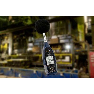 A sound level meter shows a reading of 124.6 dB in a factory environment. Background blurred, focus on measuring device.