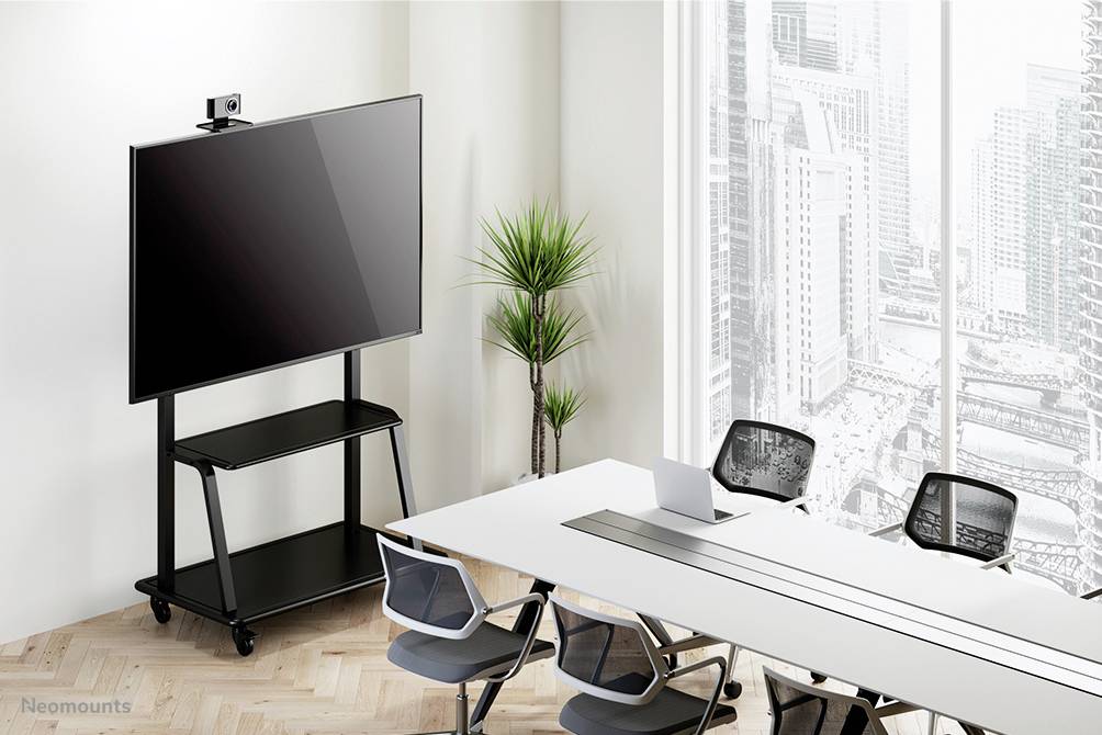 The conference room features a large screen on a mobile stand, a long table with black chairs, and a window with a city view.