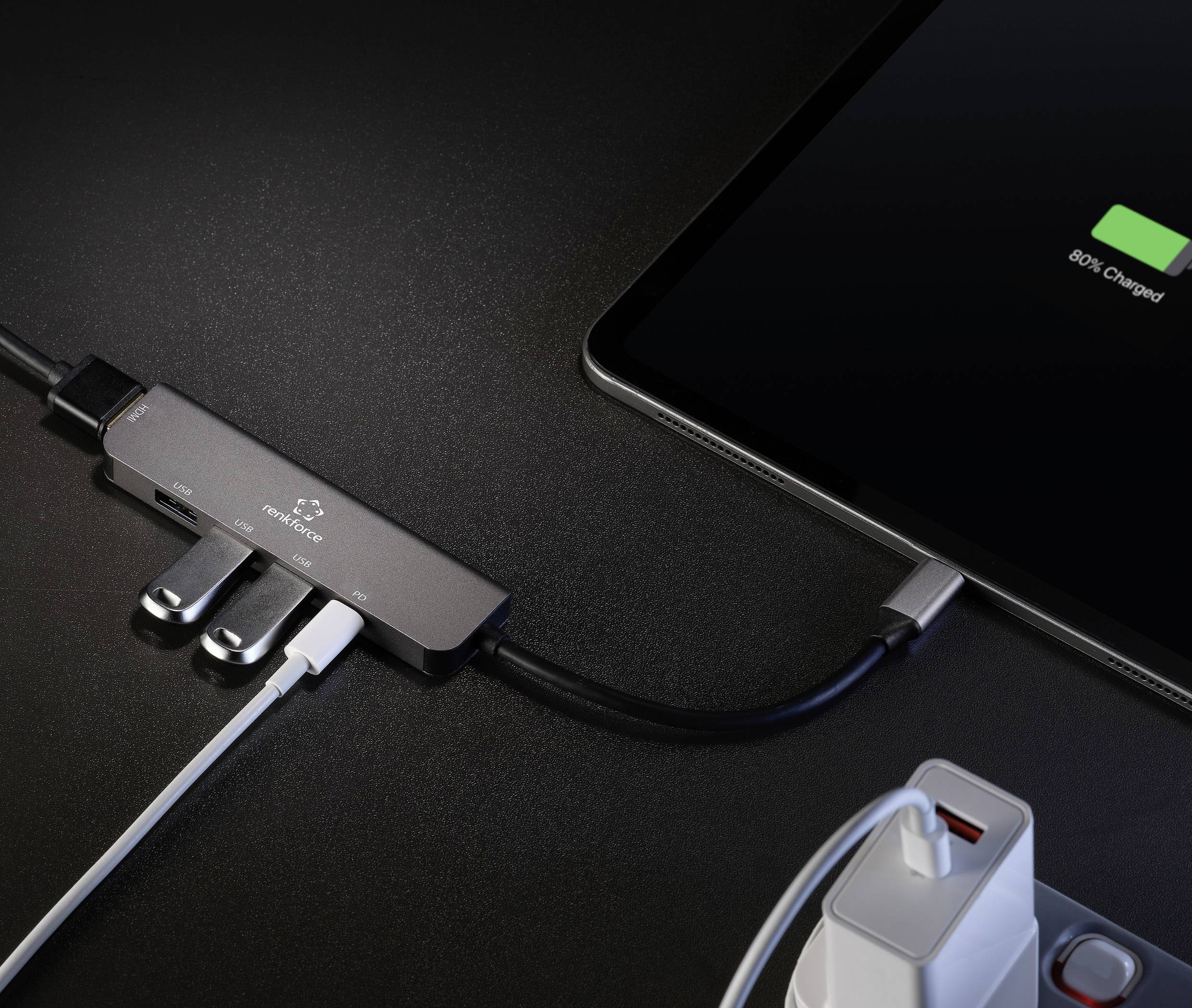A tablet is being charged via a USB hub connected to various cables. The tablet displays a 100% charge.