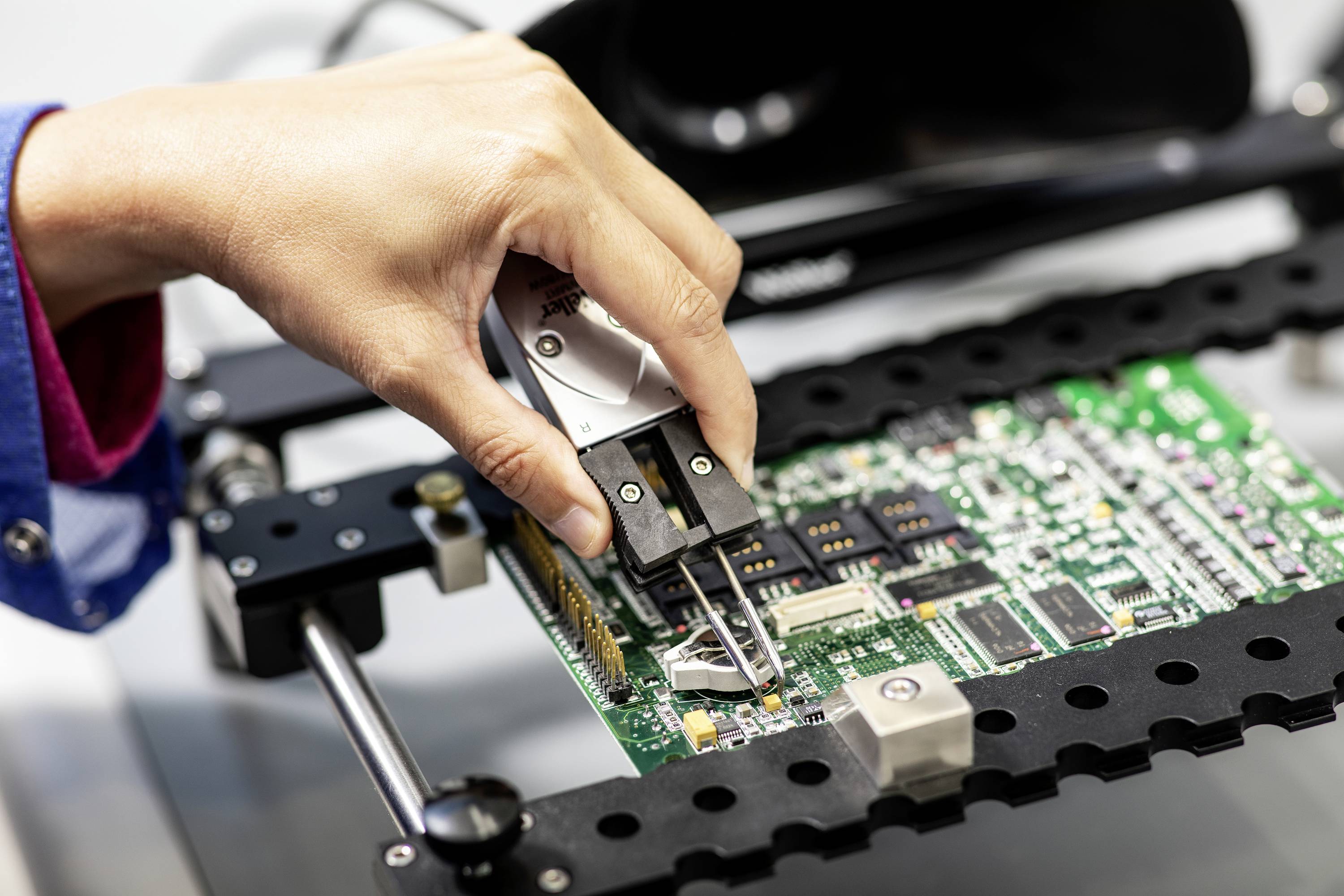 A hand calibrates a circuit board on a testing device, demonstrating technical work in the electronics sector.