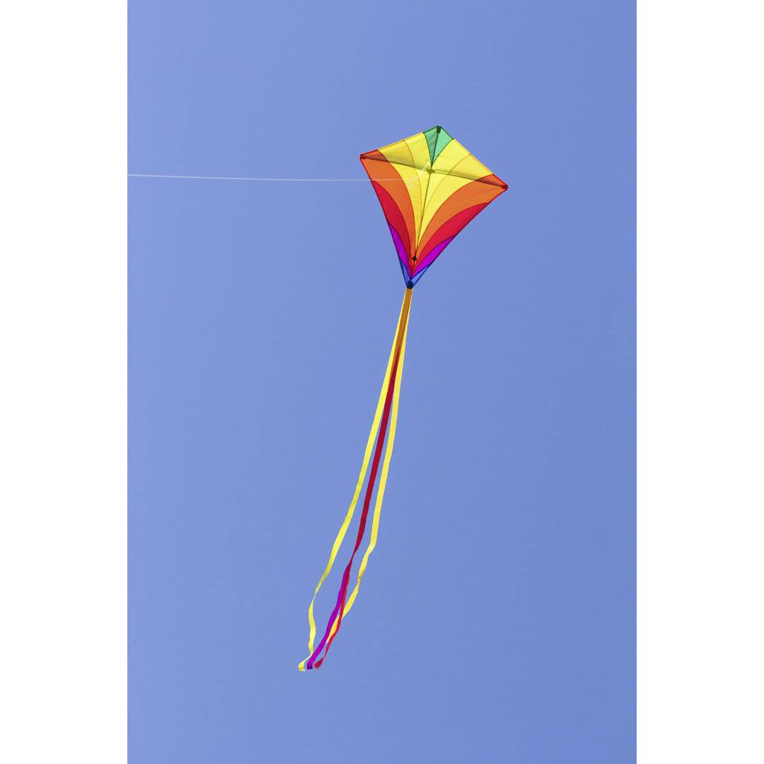 A colourful kite flies against a clear blue sky.